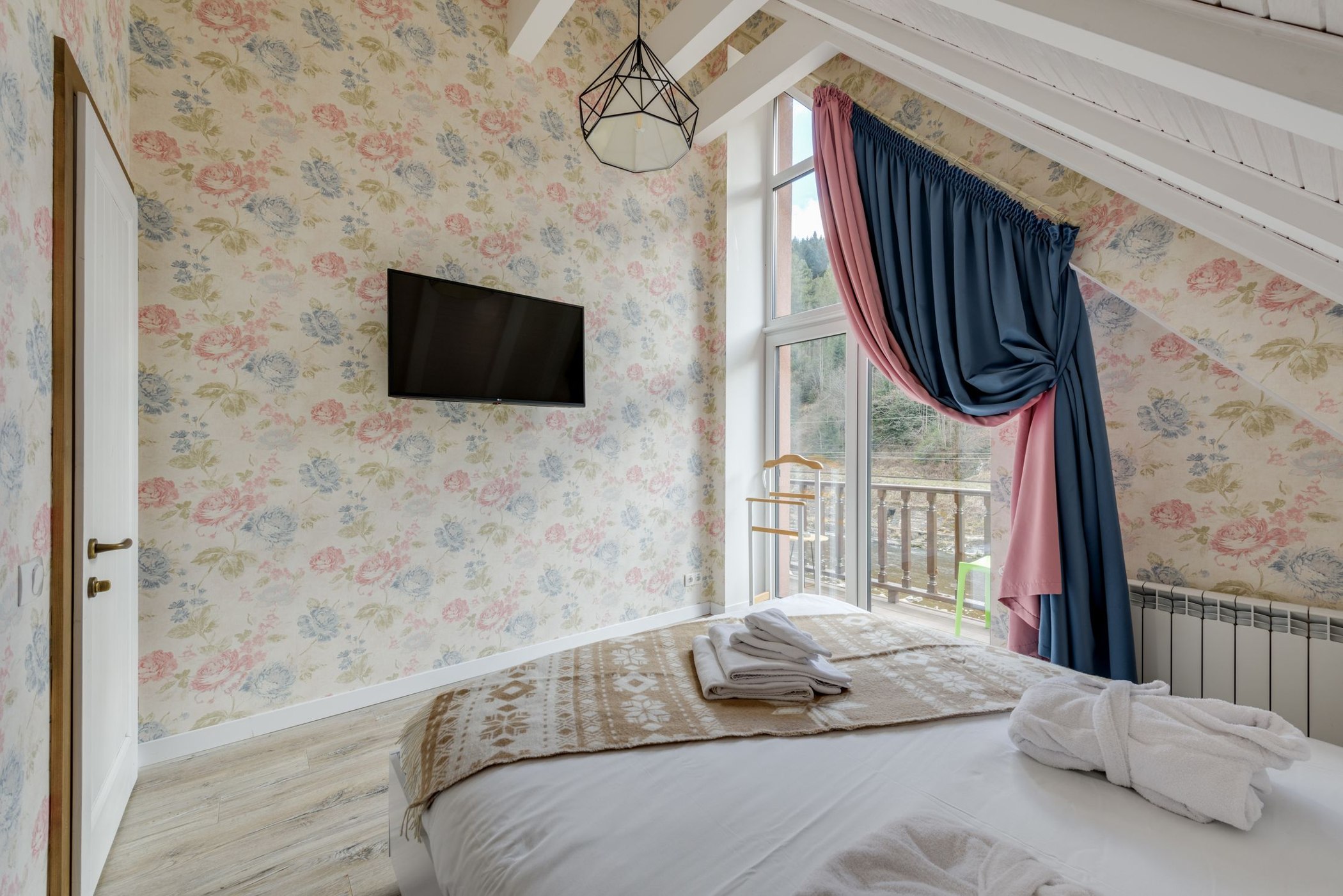 Light floral wallpaper behind a bed in a bright bedroom with exposed ceiling beams