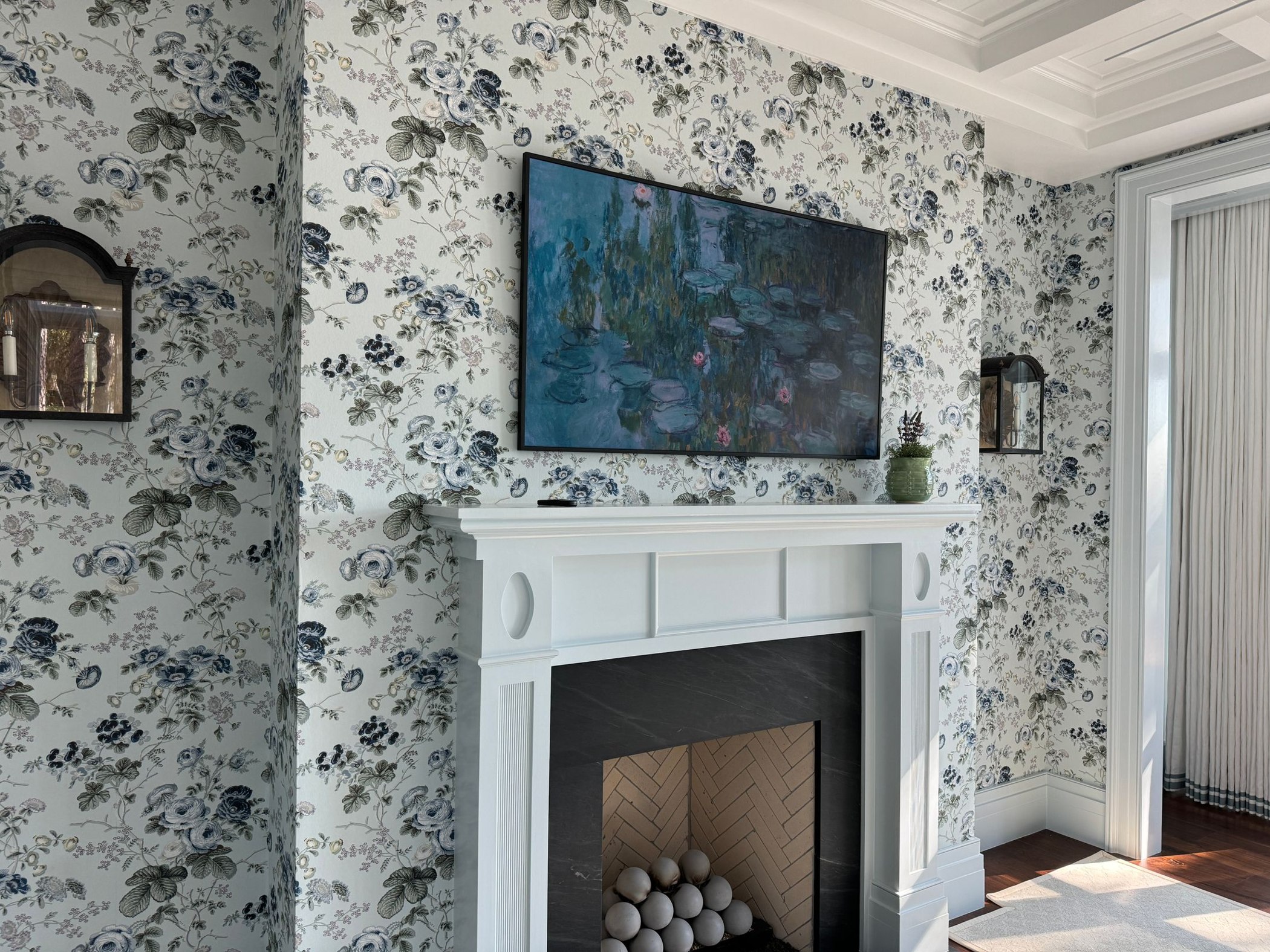Black and white botanical wallpaper installed around a white fireplace in a finished living room