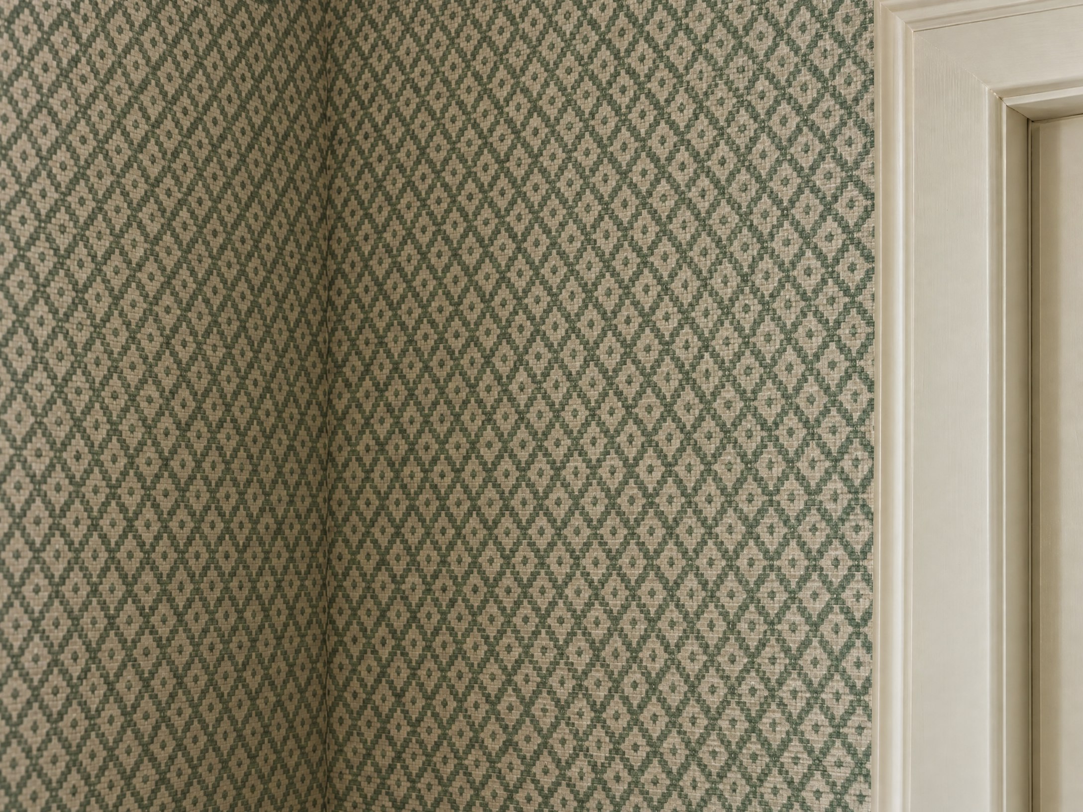 Close view of forest-green and cream geometric wallpaper carefully aligned beside interior trim